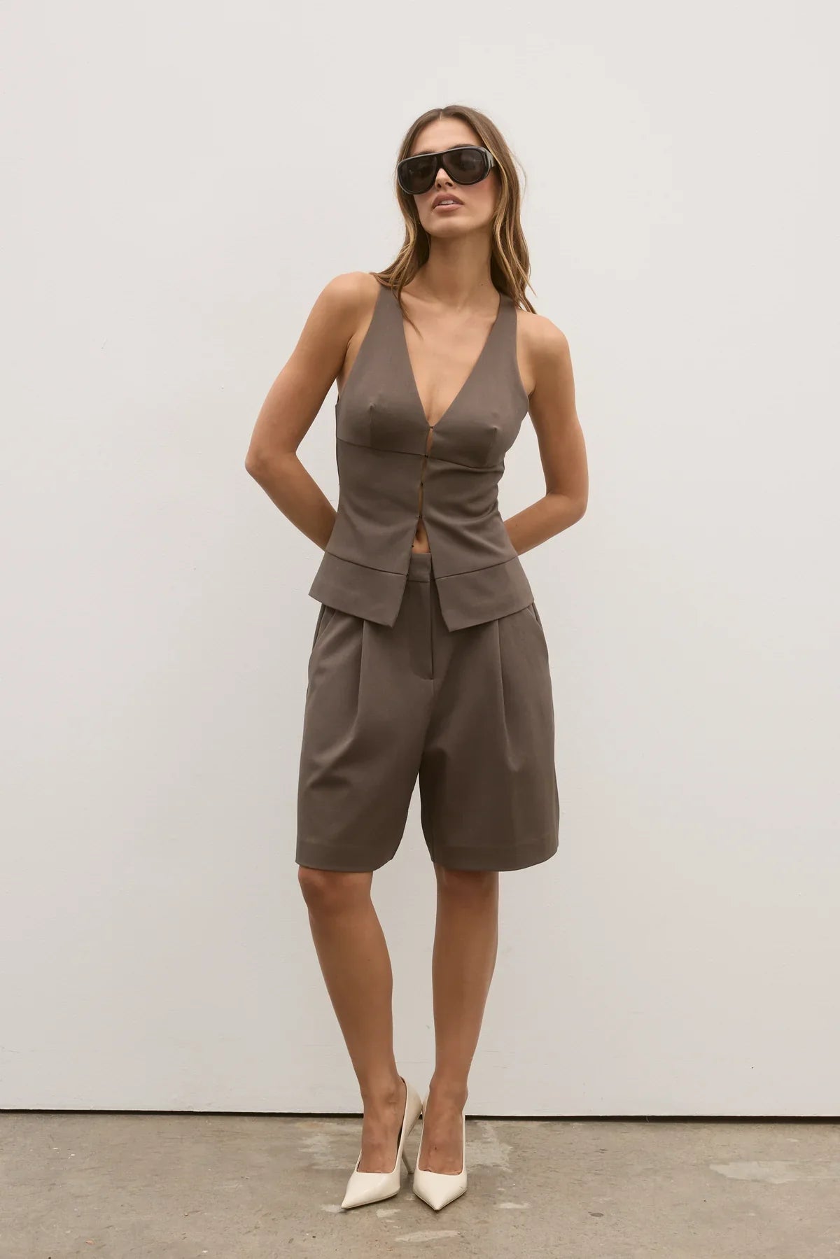 Woman wearing a brown sleeveless top and shorts set with sunglasses against a white background