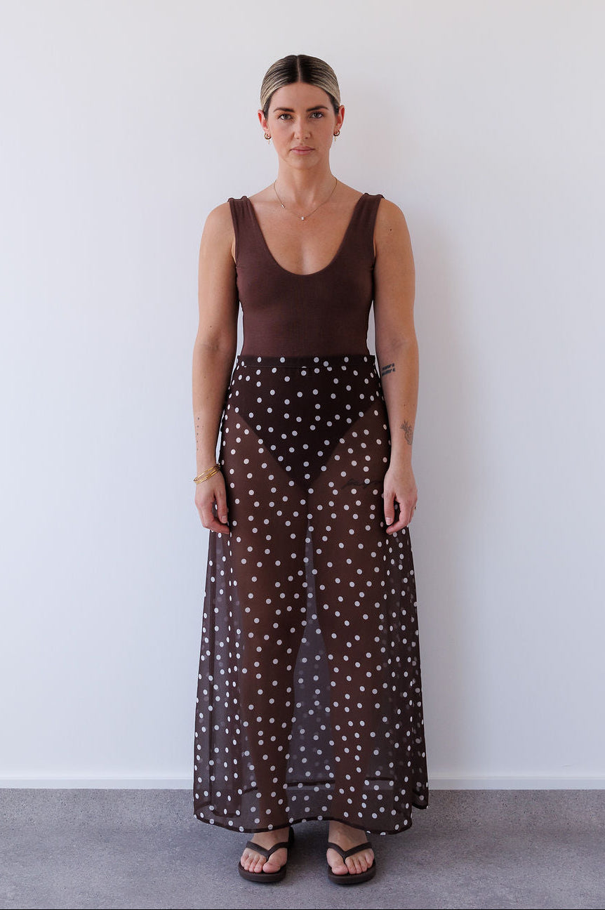 Woman wearing a brown tank top and polka dot skirt against a white background