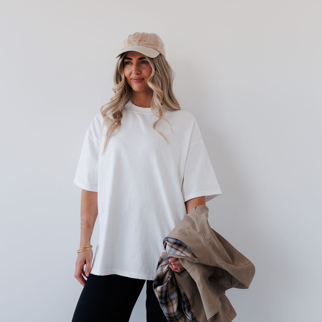Woman wearing a white t-shirt and beige cap holding a plaid blanket against a plain background