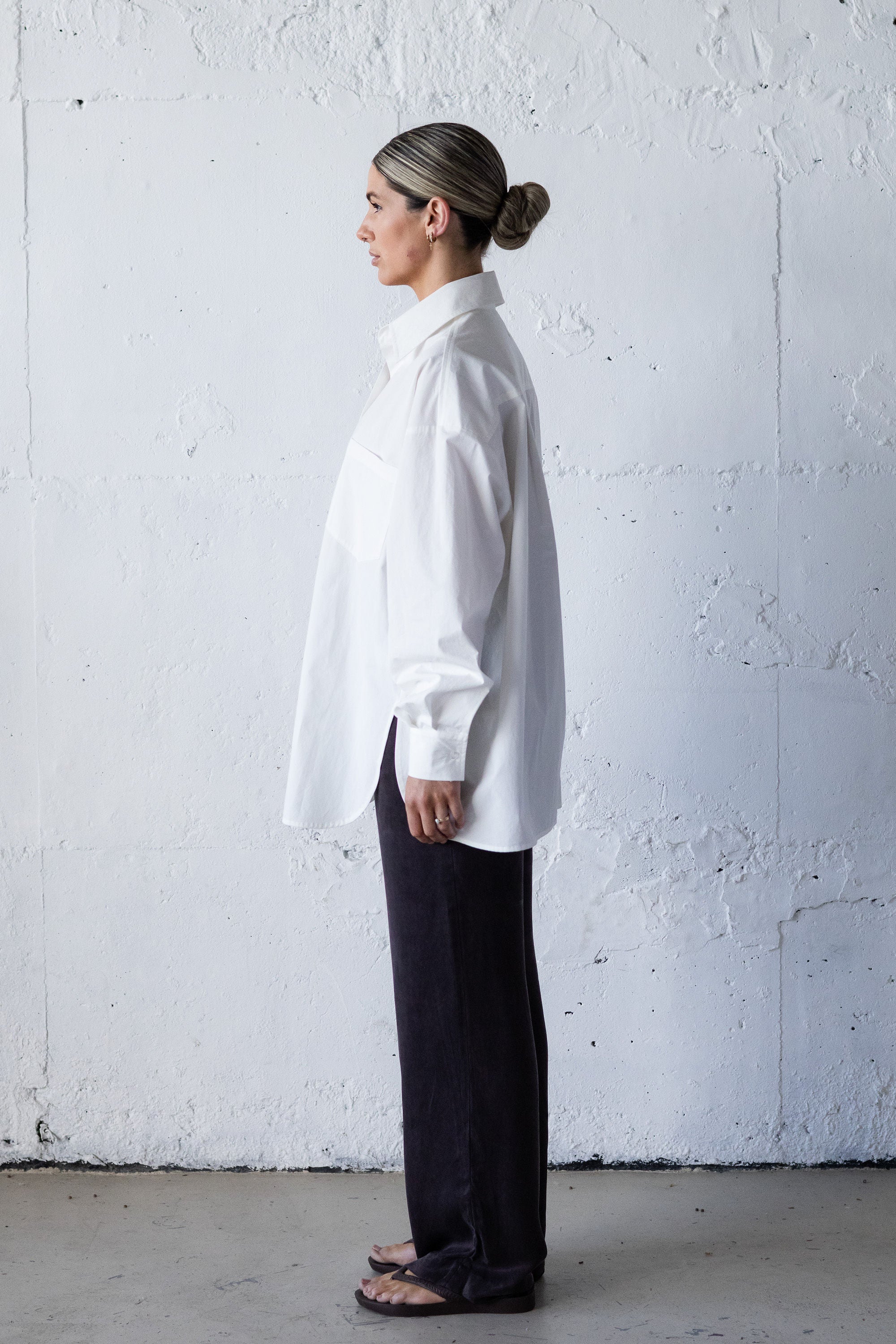 Person wearing a white shirt and dark pants against a white wall